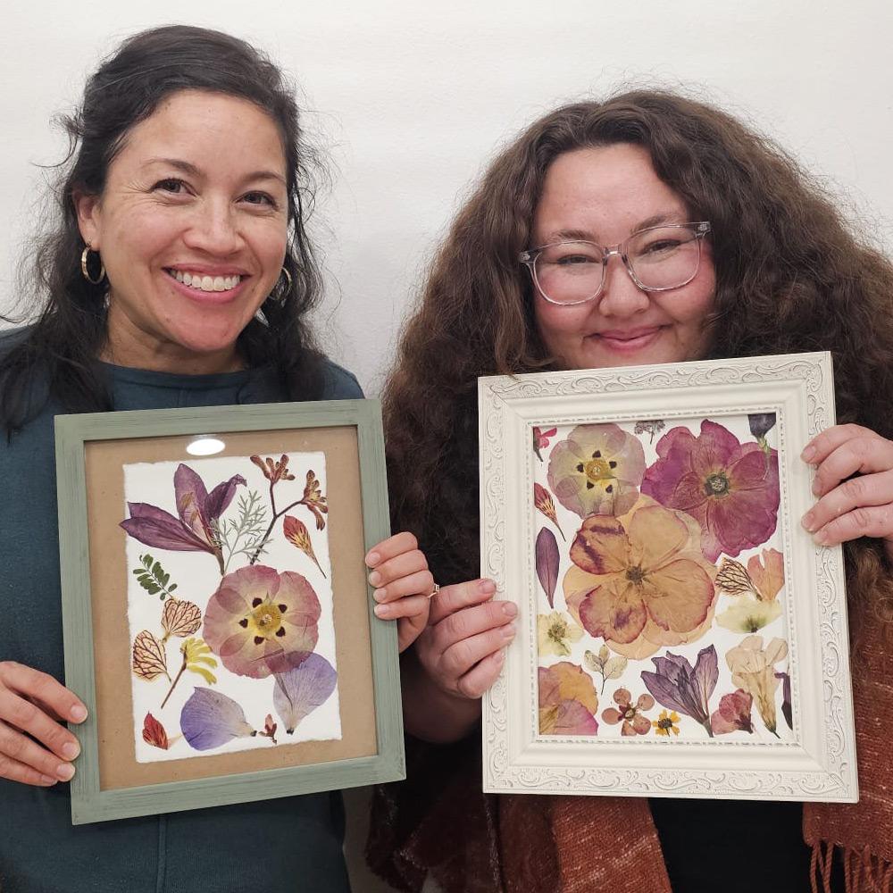 Two workshop participants holding their framed pressed flower compositions
