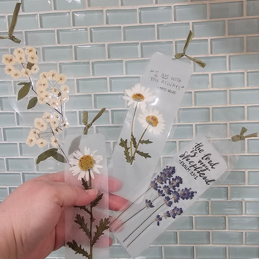 Pressed daisy and lavender bookmarks with scripture against a glass tile wall