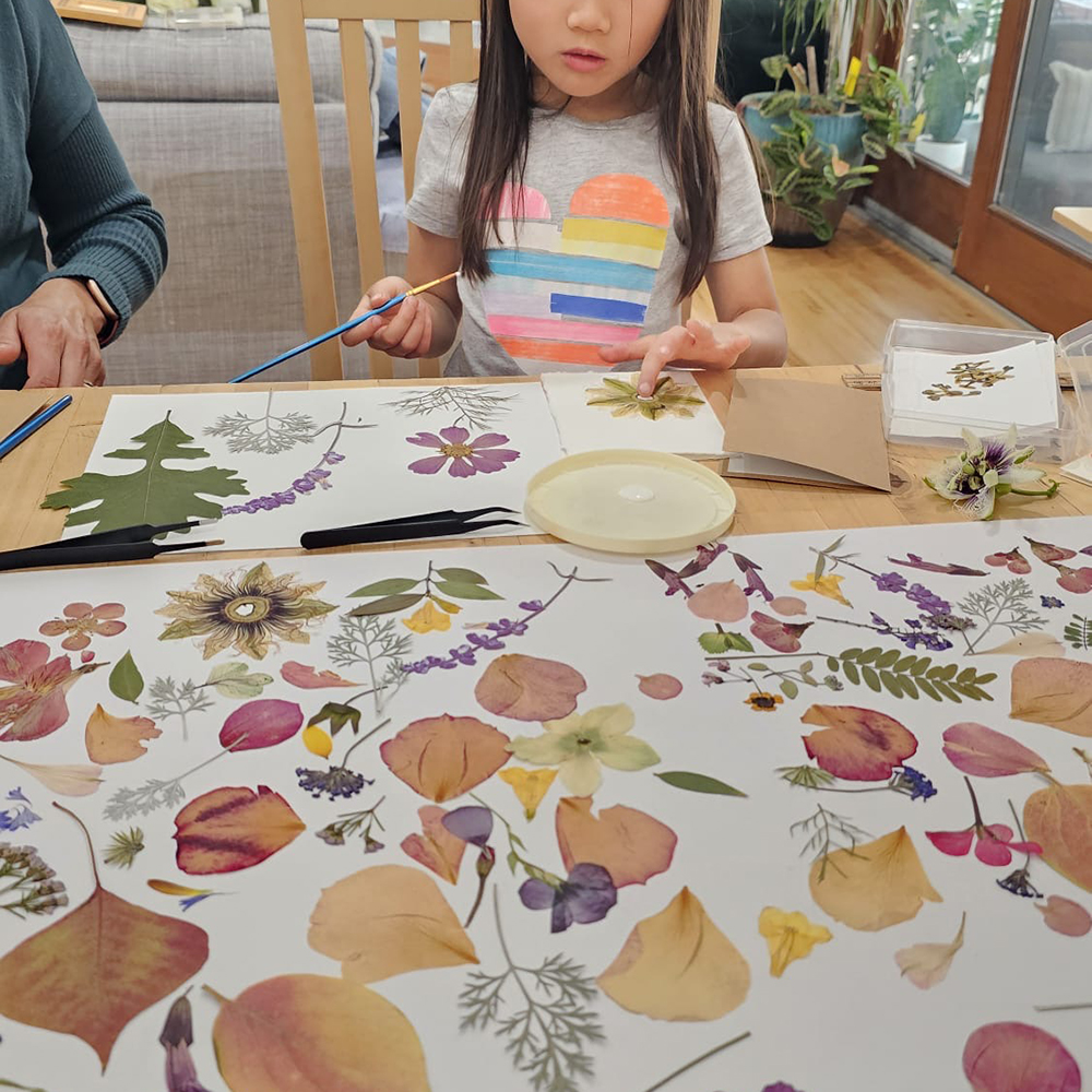 Child composing a piece at a table covered in pressed petals and leaves