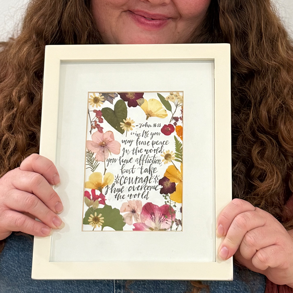 Framed calligraphy of John 16:33 surrounded by pressed flowers