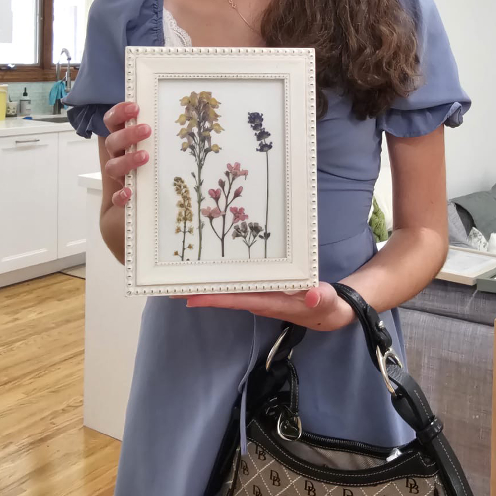 Participant holding a small white frame of pressed wildflower stems