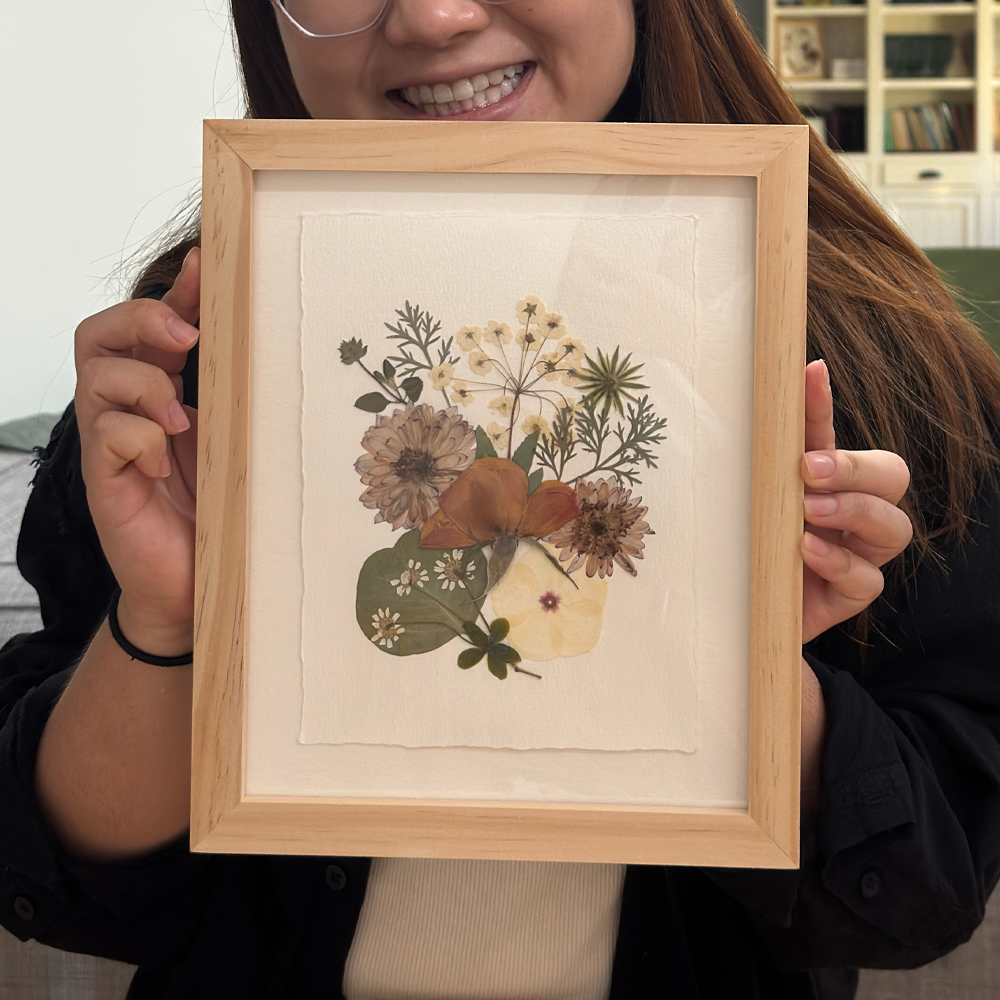 Participant holding a light wood frame with a pressed bouquet on deckled paper
