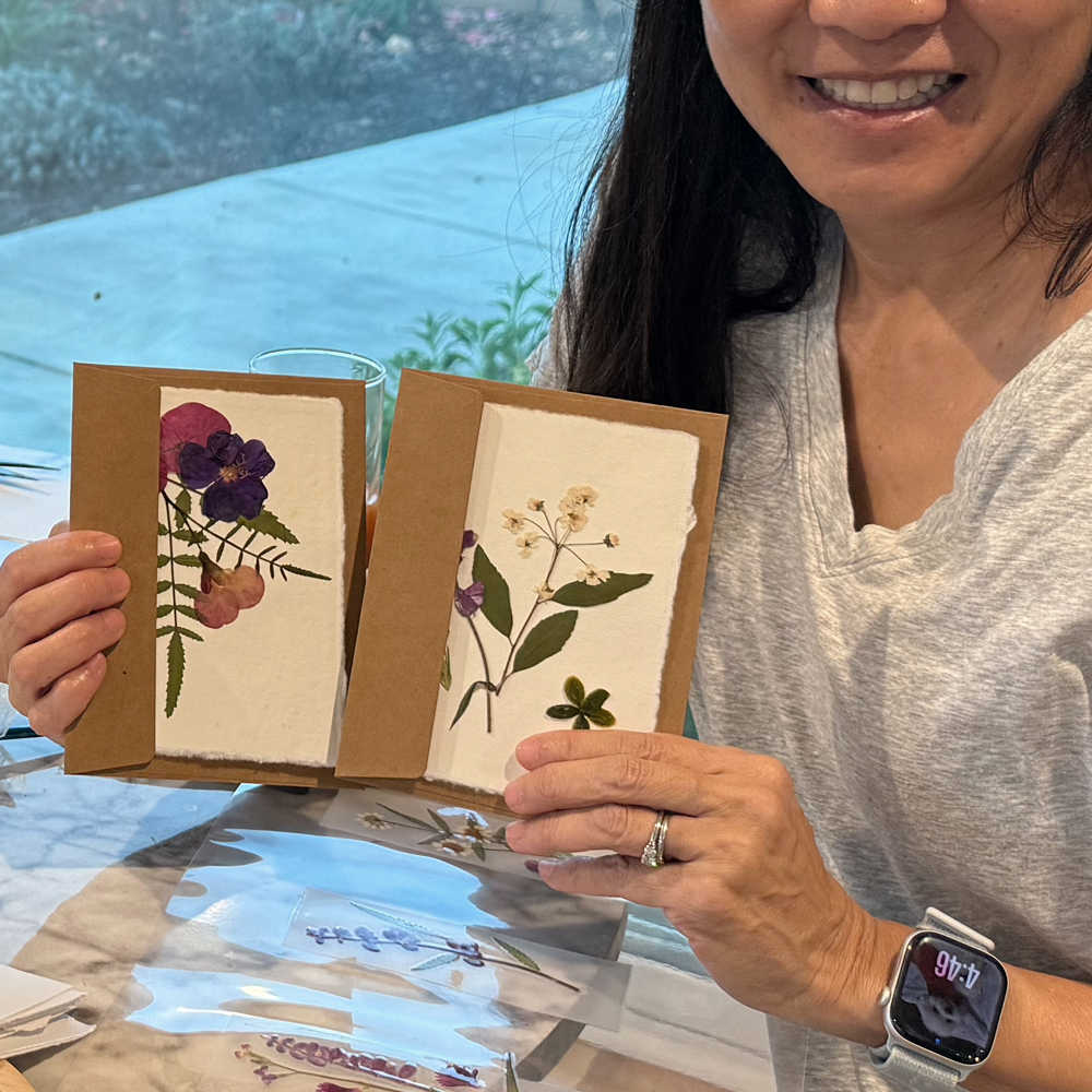 Participant holding two pressed flower cards in kraft envelopes