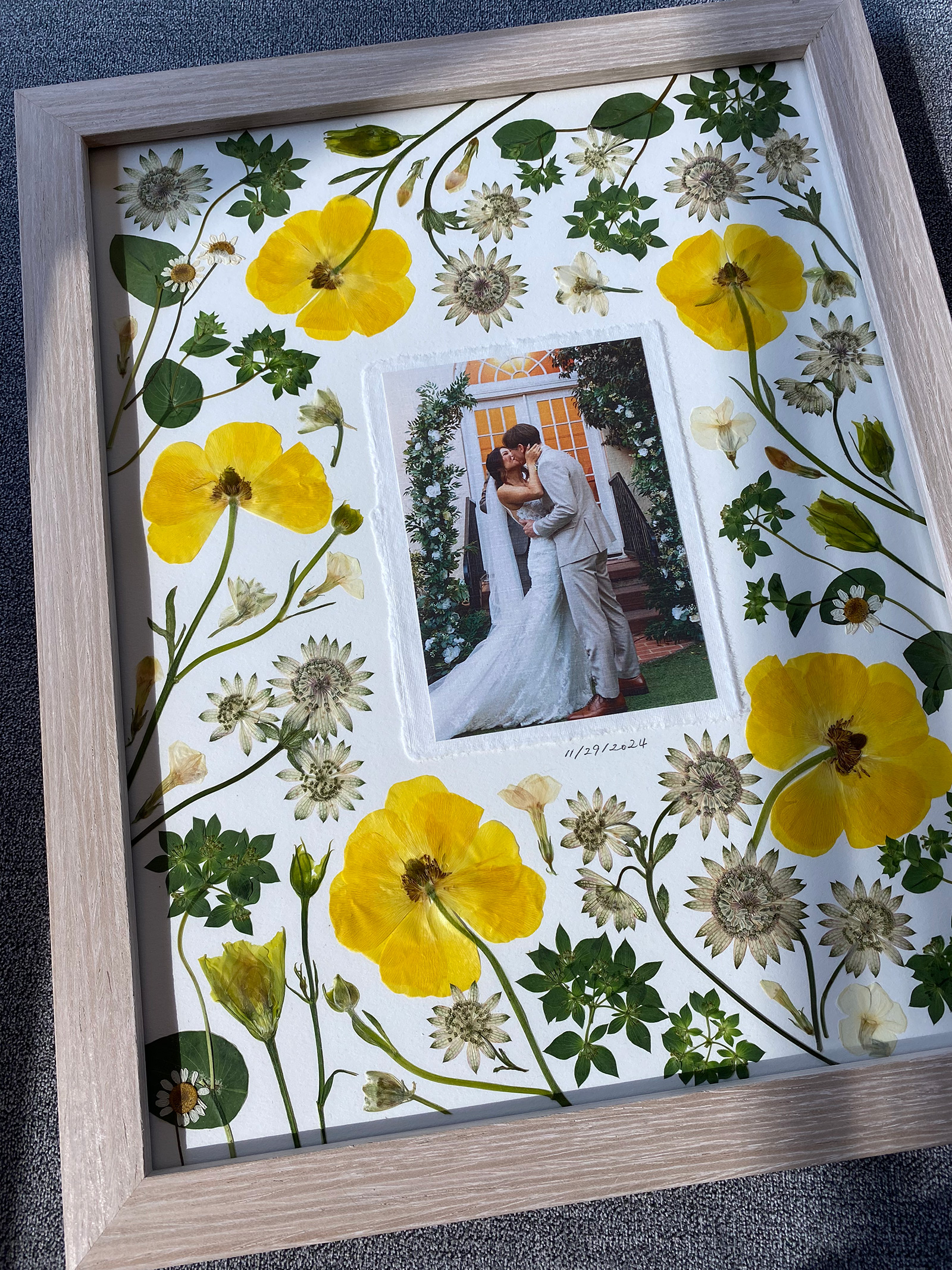 Yellow poppies and astrantia pressed around a wedding photo in a gray wood frame